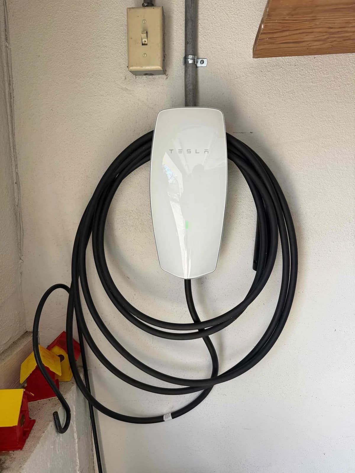 Wall-mounted Tesla EV charger with the charging cable coiled and stored against the wall