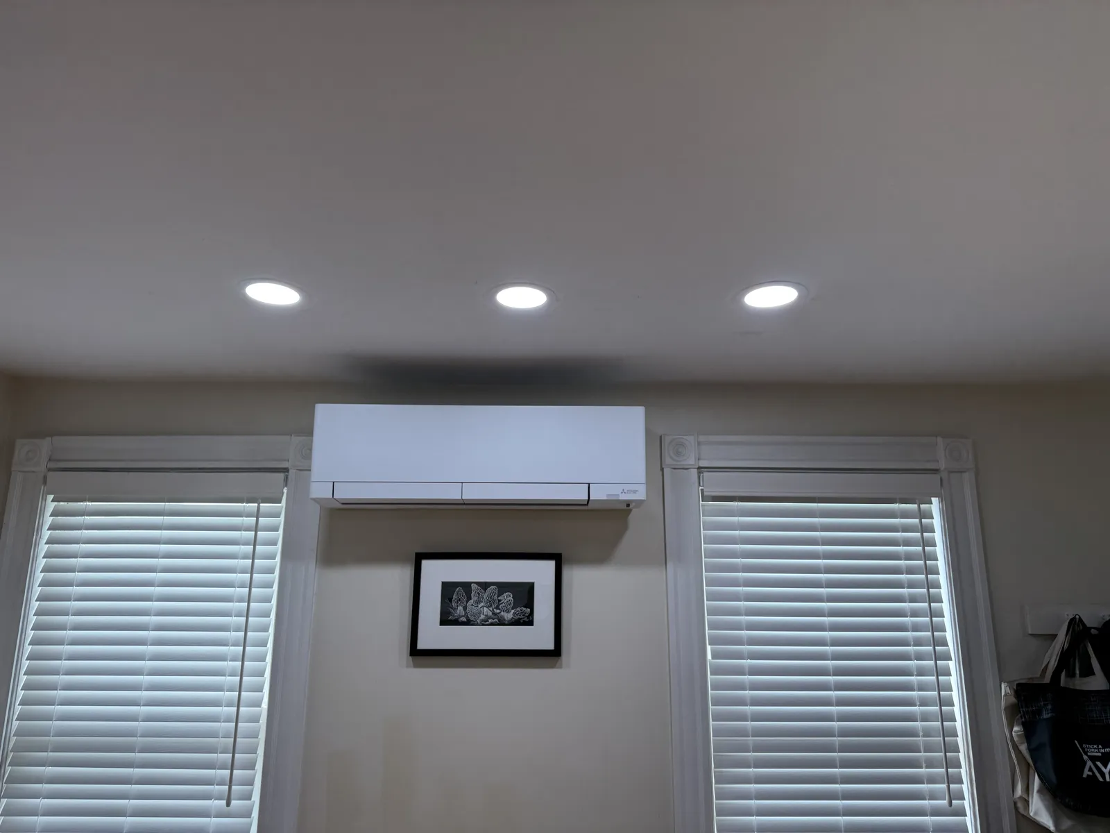 Recessed LED lights installed in a finished ceiling above windows and a wall-mounted mini-split